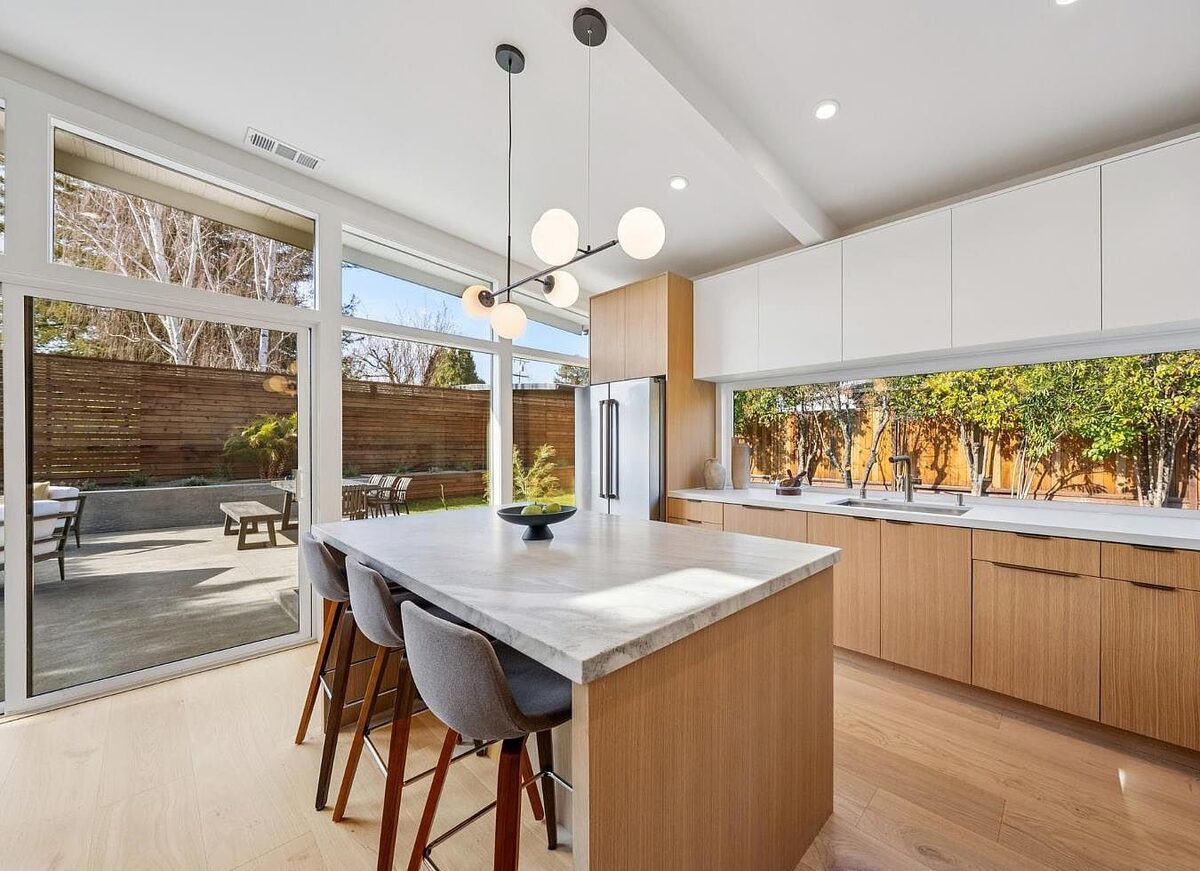 Mid-century modern kitchen with white oak cabinets and marble waterfall island, opening to the patio &mdash; DodiHome project in San Rafael